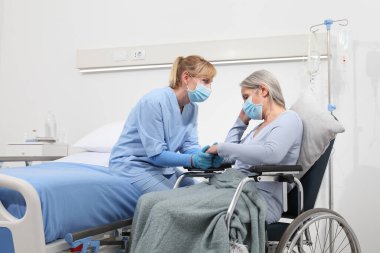 Hemşire, hastane odasında cerrahi koruyucu maskeler takan yaşlı bir kadını rahat ettirin. Corona virüsü kovid 19 'dan tecrit kavramı.