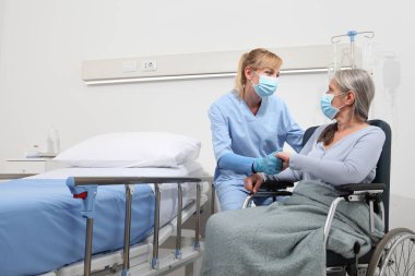 Hemşire, hastane odasında cerrahi koruyucu maskeler takan yaşlı bir kadını rahat ettirin. Corona virüsü kovid 19 'dan tecrit kavramı.