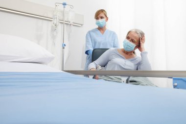 Hemşire, hastane odasında cerrahi koruyucu maskeler takan yaşlı bir kadını rahat ettirin. Corona virüsü kovid 19 'dan tecrit kavramı.