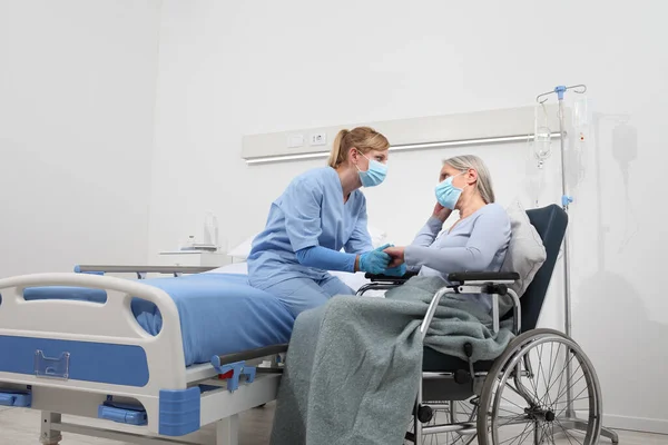 护士请坐轮椅的老年妇女放心 她戴着外科保护口罩 住在病房里 她的概念是与科洛纳病毒隔离的 — 图库照片