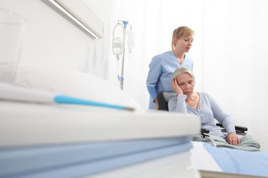 Hemşire, hastane odasının yakınındaki tekerlekli sandalyeye mahkum yaşlı bir kadına bakıyor. Yalnızlık ve yaşlılık hastalıkları kavramı.