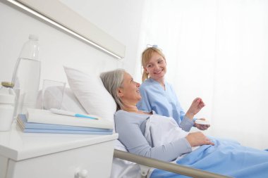 Hemşire ilacı hastane yatağında yatan yaşlı kadına, yalnızlık ve yaşlılık hastalıkları kavramına veriyor.