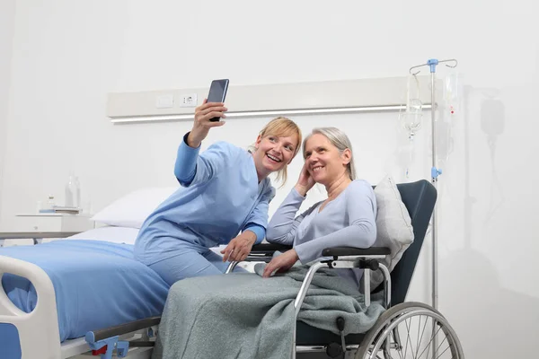 Nurse Helps Cell Phone Contact Elderly Lady Family Wheelchair Bed — Stock Photo, Image