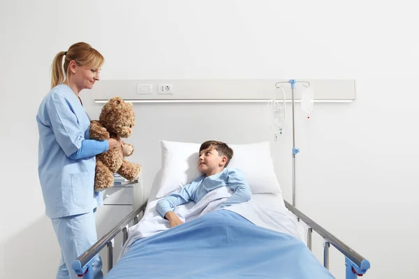 Leende Sjuksköterska Visar Nalle Till Glad Barn Ligger Sängen Sjukhusrum — Stockfoto