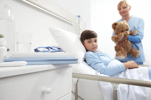 Child Lying Bed Hospital Room Looking Camera Nurse Holding Teddy — Stock Photo, Image