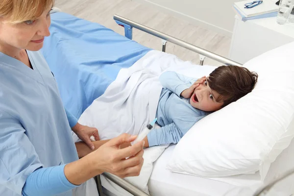 护士在给卧床躺在病房的病童注射疫苗后检查注射器的最新情况 — 图库照片
