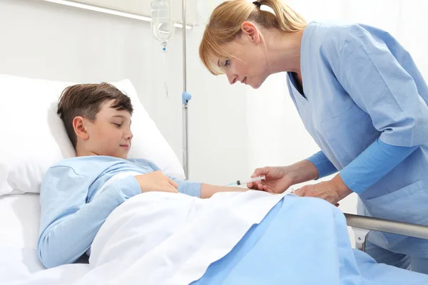 Happy child lying in bed in hospital room looking at nurse giving him an injection