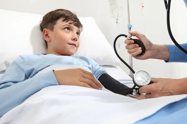 孩子躺在病房的床上 用血压计和听诊器测量他的压力 — 图库照片