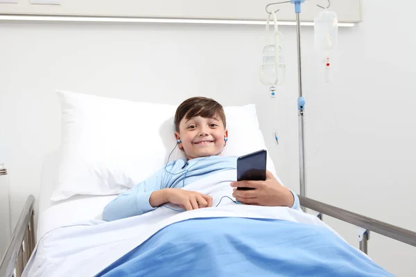 Happy Child Hospital Bed Using Smartphone Surfs Internet Wearing Earphones — Stock Photo, Image