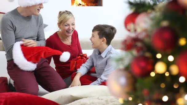 陽気なクリスマス 家で幸せな家族 両親は照明と装飾された木の近くに子供に贈り物を与え 喜びと笑顔でリビングルームに座って暖炉のそばで慰め — ストック動画