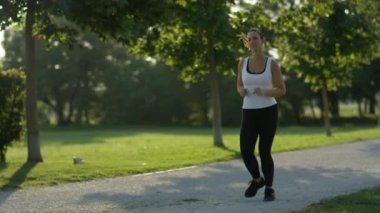 Ağır çekim Dof yakından: Koşu ve ağaçları yemyeşil park arasında şaşırtıcı güneşli akşamı egzersiz şekil çekici genç kadın. Ağaç sağlayan canlandırıcı gölge sıcak yaz sabahı Kanopiler
