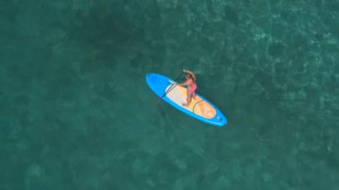 Hava, yakın: Sup tahta üzerinde duran ve çarpıcı zümrüt okyanusta şaşırtıcı güneşli günde kürek çekmeye pembe bikini çekici genç kadın sörfçü yukarıda uçan. Joy ride ve rahatlatıcı yaz tatili