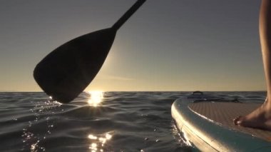 Ağır çekim, Close Up: sıkıca şişme Sup tahta üzerinde duran ve kürek çekmeye kadın. İterek ve su yüzeyi parlayan ve iten paddleboard güneşli sabahı kürek çekerek eller