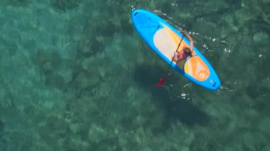 Hava: güzel kız binici standup paddleboarding güzel berrak turkuaz tropikal deniz içinde yukarıda uçan. Çarpıcı kayalık, taşlık ve kumlu deniz dibinin açığa delici şeffaf su güneş ışınları