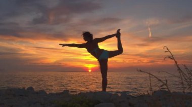 Yakın: Kral Deniz büyülü altın ayarı gökyüzü altında dalgalanan tarafından çarpıcı kayalık plaj konumuna dansçı Dengeleme güçlü kız. Kadın ayakta Yoga bacak tek elle tutarak köprü ile poz