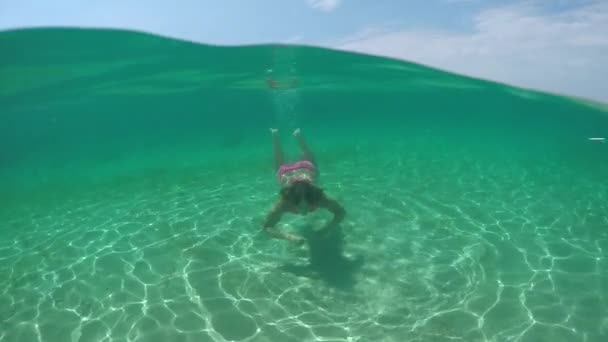 クローズ アップ スローモーション水中 魅力的な若いブルネットの少女ラグーンの透明な海でダイビングします 太陽光浸透水表面および見事な白い砂浜の海の底に反射 — ストック動画