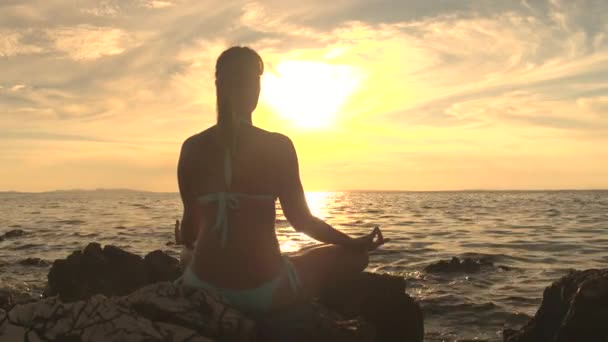 クローズ アップ 若い女性波打つ海 ロータス ヨガのポーズで瞑想 沈黙の中で集中して岩の上に座って観察息 魂と体をリラックスします 禅の調和に到達しようとして穏やかな女性 — ストック動画