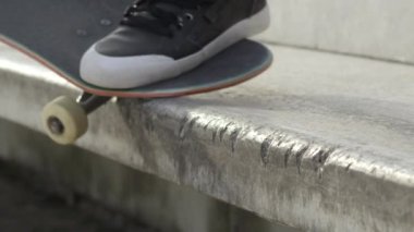 Ağır çekim Dof aşırı yakından: atlama ve sokakta beton bankta sürgülü tanınmaz kaykaycı. Patencinin kaykay bacaklar ve hile bir şehirde kaykay ile taşlama iş closeup