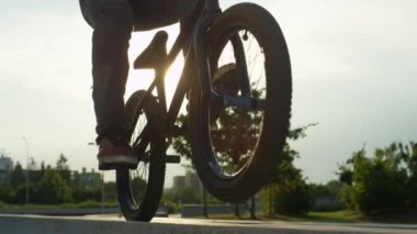 Ağır çekim Dof yakından: Park beton bir bankta sürme ve güneşli günde arka tekerlek üzerinde bisiklet aşırı bmx motorcu. Güzel yaz günü Wheelie hile yaparak havalı motorcu