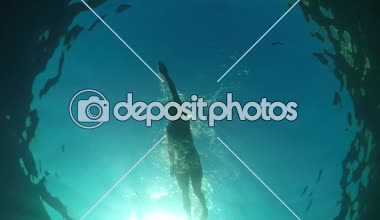 Ağır çekim yakın sualtı düşük açı bakış: kas adam yüzme serbest vuruş inanılmaz açık okyanusta çarpıcı güneşli yaz gününde uygun. Kristal berraklığında su ve deniz yüzeyi penetran güneş ışığı