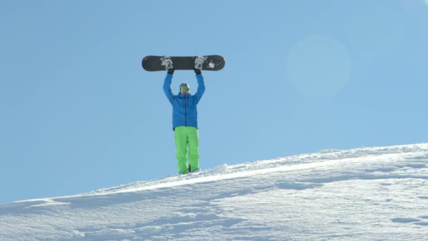 極端なスノーボーダー上り坂ハイキング 山の頂上に到達 誇らしげにスノーボードを上げます フリーライド スノーボーダーが雪に覆われた山頂に到達マウンテン スキー リゾートで正常に彼のスノーボードを上げる — ストック動画