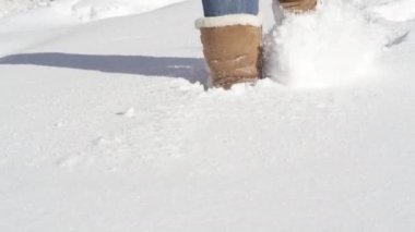 Ağır çekim yakın çekim: Tanınmayan kadın kot pantolon ve sıcak kış çizmeleri pürüzsüz derin kar battaniyeye yürüme. Taze kar üzerinden güzel bir güneşli Noel günü gölet ve göllerde kadında koyun derisi çizmeler