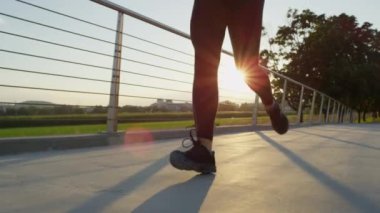 Ağır çekim yakın çekim: aktif erkek arka planda yüksek binalar ile küçük banliyö kasabasında güzel yeşil park içine çelik köprü üzerinden çalışan. Sportif kız taze yaz sabahı koşu