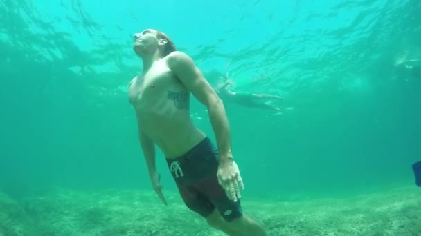 慢动作 运动男子潜水在美丽的绿松石海底部尖锐的岩石海底 游泳到表面喘口气 人摇摇头 水滴飞溅 — 图库视频影像