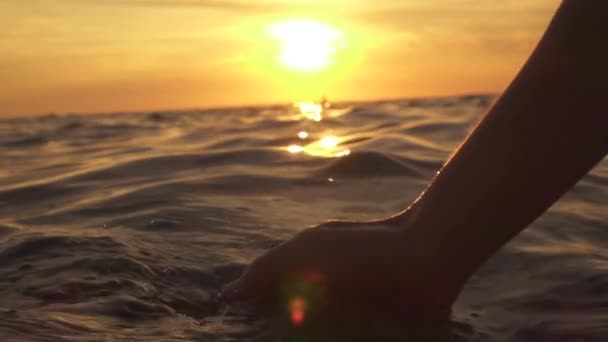 スローモーション クローズ アップ 被写し界深度 女性彼女の手に滑らかな塩辛い水をすくい ドロップ 水滴の飛散 打撃の光沢のある海面 夢のような黄金の夕日で海で遊ぶ少女 — ストック動画