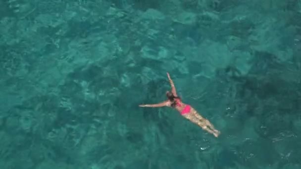 迷人的白种女孩游泳和环顾四周美丽的绿松石水晶清澈的海洋 阳光穿透波光粼粼的水揭示惊人的岩石和沙海底部 — 图库视频影像