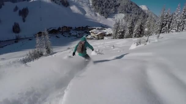 Nahaufnahme: junge Snowboarderin auf frischem Pulverschnee im sonnigen Winter. Freeride-Snowboarderin beim Snowboarden im perfekten Pulverschnee abseits der Piste in Richtung Dorf im Bergskigebiet.