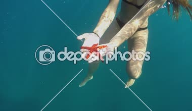 Ağır çekim yakın sualtı çekim: Tanınmayan kadın güzel kırmızı denizyıldızı onun elinde tutan ve bunu erkek arkadaşına göstermek masmavi okyanusta yüzmeye bikini. Egzotik Adası'nda çarpıcı deniz yaşamı
