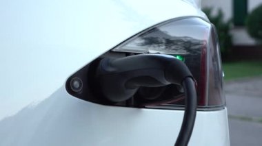 Yakın: elektrikli otomobil ne zaman pil tam şarj istasyonu üzerinden bağlantısını kesme tanınmayan adam. Şarj lüks beyaz Tesla araba elektrik. Kabloyu prizden ne zaman pil dolum komple