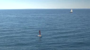 Hava, yakın: uygun genç kız sörfçü masmavi okyanusta şişme standup paddleboard sürme ve tekne yelken üzerinde gözlemleyerek pembe bikini güneşli çarpıcı yaz günü dalgalar mutlu uçan