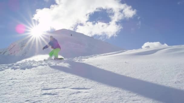 Zeitlupe aus nächster Nähe: Extrem-Snowboarder fahren Powder und ziehen mit der Hand, versprühen Schnee über die Sonne im sonnigen Gebirgsbackcountry. Snowboarder beim Snowboarden im Neuschnee abseits der Piste