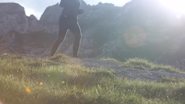 慢动作特写 在阳光明媚的夏日 有权势的年轻女性在山上奔跑 美丽的登山小路上有岩石和草地 微笑活泼的女孩徒步旅行 在洛基山脊上慢跑 — 图库视频影像