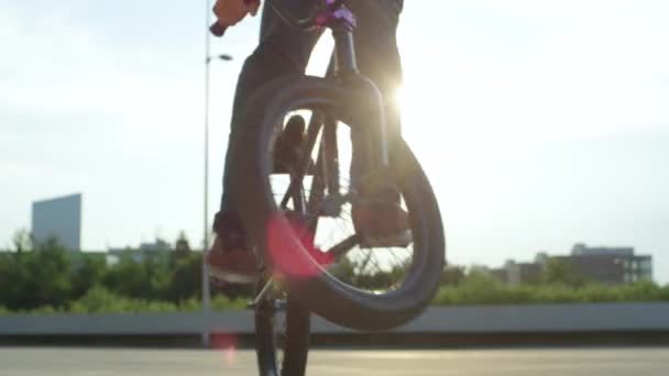 スローモーションをクローズ アップ 極端な Bmx バイク ペダルと美しい夏の日当たりの良い公園でウサギのホップ トリックをジャンプします オリーに晴れた日に都市公園の日没の太陽の上のトリックを行う若い Bmx バイクをクールします — ストック動画