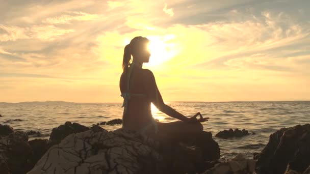 クローズ アップ 若い女性波打つ海 ロータス ヨガのポーズで瞑想 沈黙の中で集中して岩の上に座って観察息 魂と体をリラックスします 禅の調和に到達しようとして穏やかな女性 — ストック動画