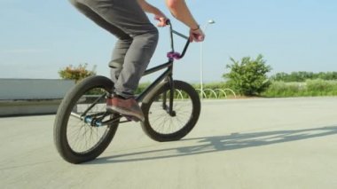 Ağır çekim yakın çekim: pedal ve atlama bunny hop hileler güneşli Park Yaz aylarında aşırı bmx motorcu. Hile ve şehir parkı 360 rotasyon güneşli Ollie yapıyor genç bmx motorcu serin