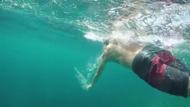 クローズ アップ スローモーション水中 認識できない男水泳自由形ストロークや美しい晴れた日に驚くべきのターコイズ ブルーの海でリラックスします 水滴飛散や ガラスの水表面の上に落ちて — ストック動画