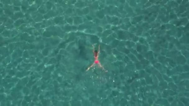 迷人的年轻白种女人在比基尼游泳下在美丽的绿松石海洋表面 阳光穿透波光粼粼的透明水 露出令人惊叹的岩石和沙滩海底 — 图库视频影像
