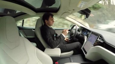 Yakın: kırsal yol boyunca seyahat özerk otomatik pilot sürücüsüz elektrikli otomobil içinde kendi kendine sürüş direksiyon arkasında otururken cep telefonunda mesaj yazarken genç işadamı manifatura