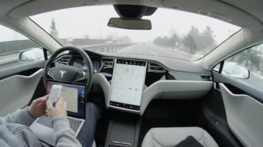 Özerk araba - 4 Şubat 2017: direksiyon tutun ve karayolu üzerinde kontrol altına almak için sürücü dikkat talep Self-driving Tesla Model S araba otomatik pilot. Laptop ve cep manifatura üzerinde çalışan adam