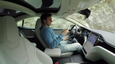 Erkek sürücü kırsal yol boyunca seyahat özerk otomatik pilot sürücüsüz elektrikli otomobil içinde kendi kendine sürüş direksiyon arkasında oturan Smartphone cep telefonu ile mesaj yazarken. Araçtaki adam manifatura