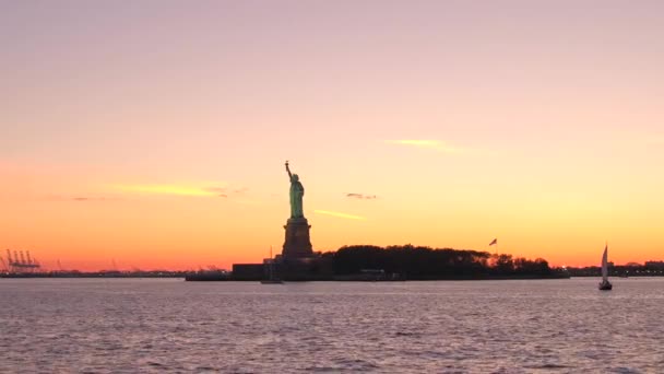 象徴的な女神 息をのむ黄金夕焼け空に対してニューヨーク港でリバティ島自由国定の像 ニューヨークの夕暮れ時に有名な壮大な銅彫刻 — ストック動画