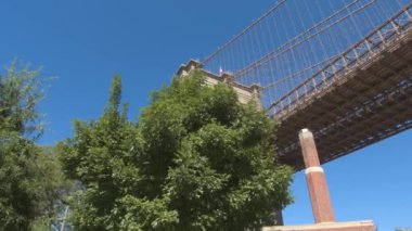Ağır çekim, düşük görüş açısı, Close Up: Tarihi Brooklyn Bridge çevrili yemyeşil yeşil ağaç Kanopiler karşı çarpıcı mimari tasarımının ayrıntılarını temizleyin mavi gökyüzü güneşli günde New York'ta