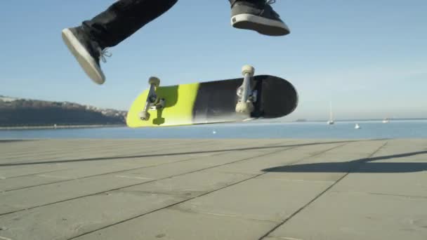 スローモーション クローズ アップ 被写し界深度 認識できないスケート スケート ボードと日当たりの良い夏の海沿いの遊歩道に 360 フリップ トリックをジャンプします — ストック動画