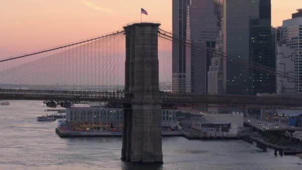 象徴的なブルックリン橋を見渡せる美しいピンクの夜明けにマンハッタン橋を運転します モダンなガラスの高層ビルとバック グラウンドでダウンタウン マンハッタン ビジネス地区の事務所ビル — ストック動画
