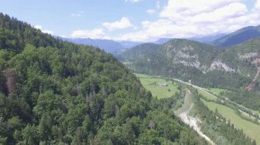 Hava: yeşil vadi Çam ormanıyla kaplı güneşli yaz gününde aracılığıyla kıvrımlı Nehri üzerinde uçan. Küçük kasaba eteklerinde arka plan dağlarda kar başlıklı ile lider dolambaçlı yol