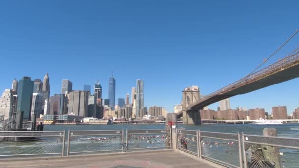 低角度のビュー ブルックリン橋の象徴的な表示やダウンタウンの高い現代的な高層ビル フェリーからマンハッタンをドッキングします ニューヨーク市のマンハッタンとブルックリンの自治区を接続するブルックリン橋 — ストック動画